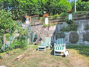 Un patio trasero con dos sillones reclinables a rayas, un perro y un muro de piedra con plantas.
