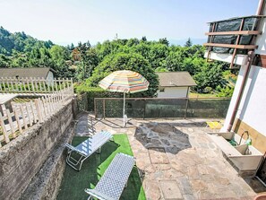 A rooftop terrace with a small table, a colorful umbrella, and a view of a forested area.