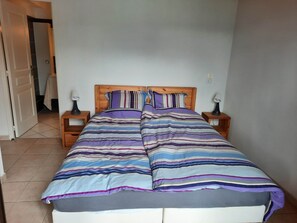 Ein Schlafzimmer mit einem Bett, zwei Nachttischen und einer Tür zu einem weiteren Raum.