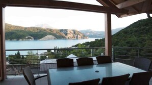 A terrace with a table and chairs overlooking a lake and mountains. - Breathtaking view of Lake Serre-Ponçon (Chorges)