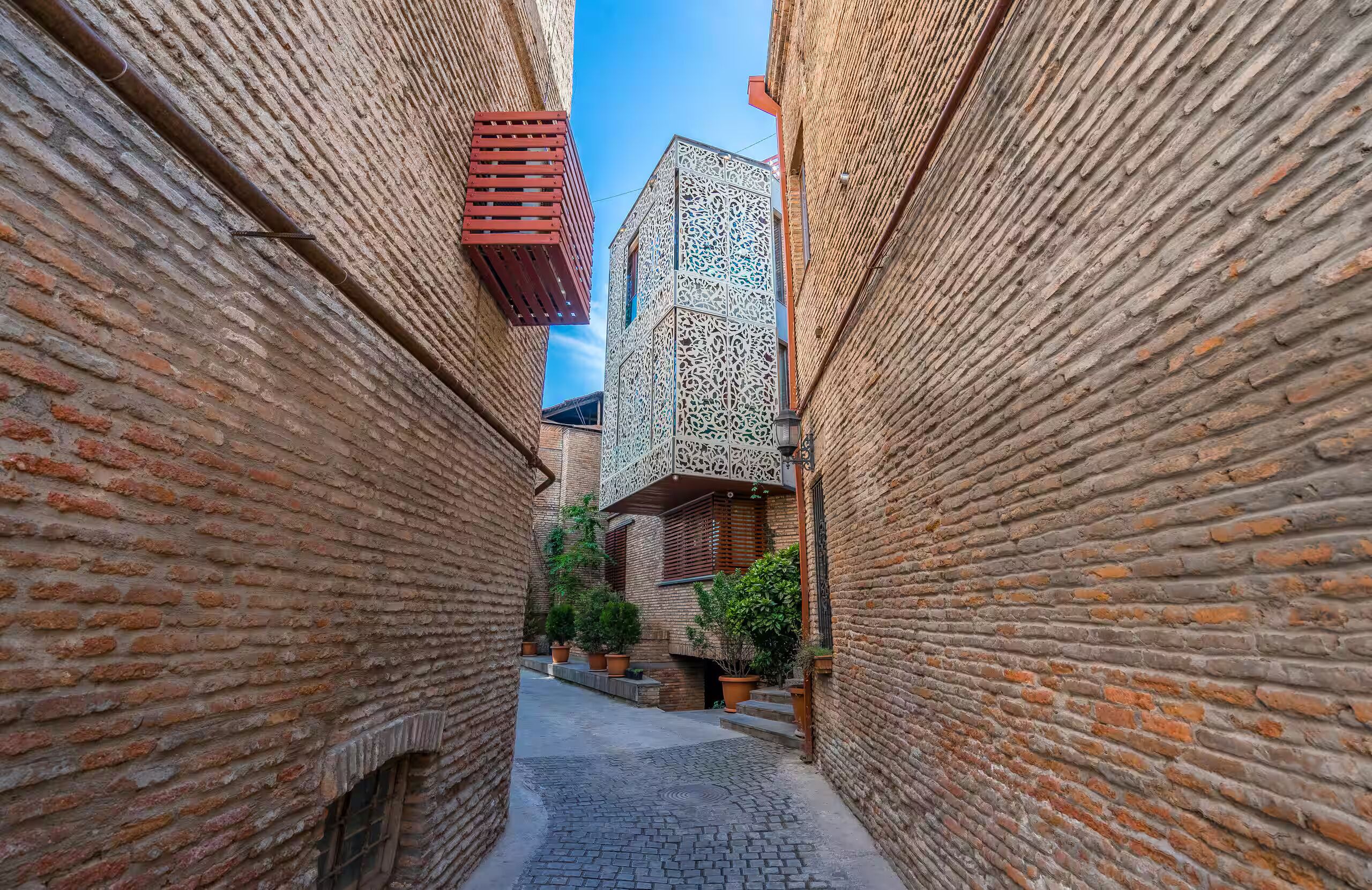 Une ruelle étroite entre deux immeubles en briques, dont la façade présente un motif décoratif, avec un ciel bleu clair au-dessus.