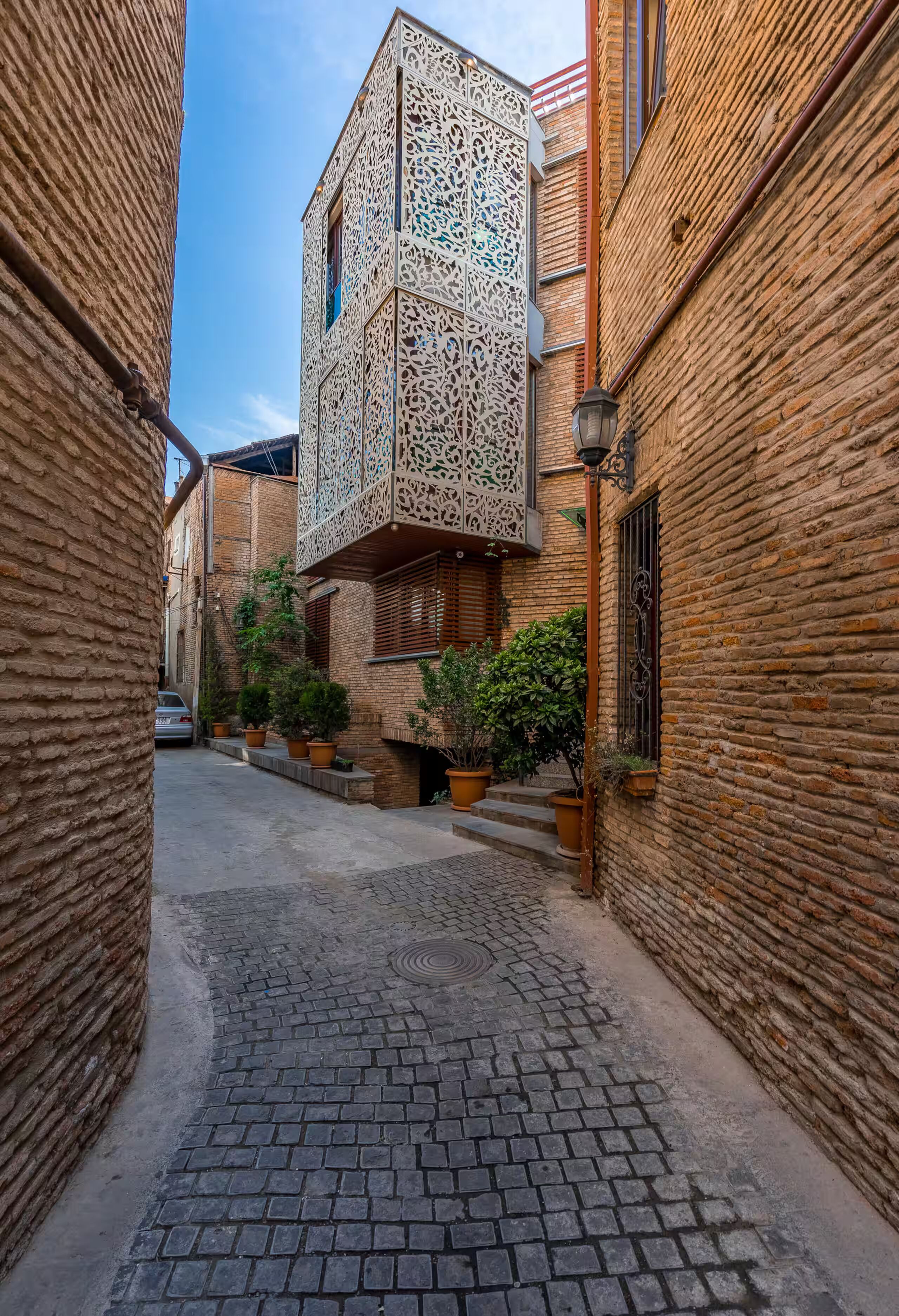A narrow cobblestone alley with brick buildings, one featuring intricate white lattice work.