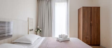 Hotellihuone, jossa on sänky, vaatekaappi, ikkuna verhoilla ja seinälle ripustettu taideteos.