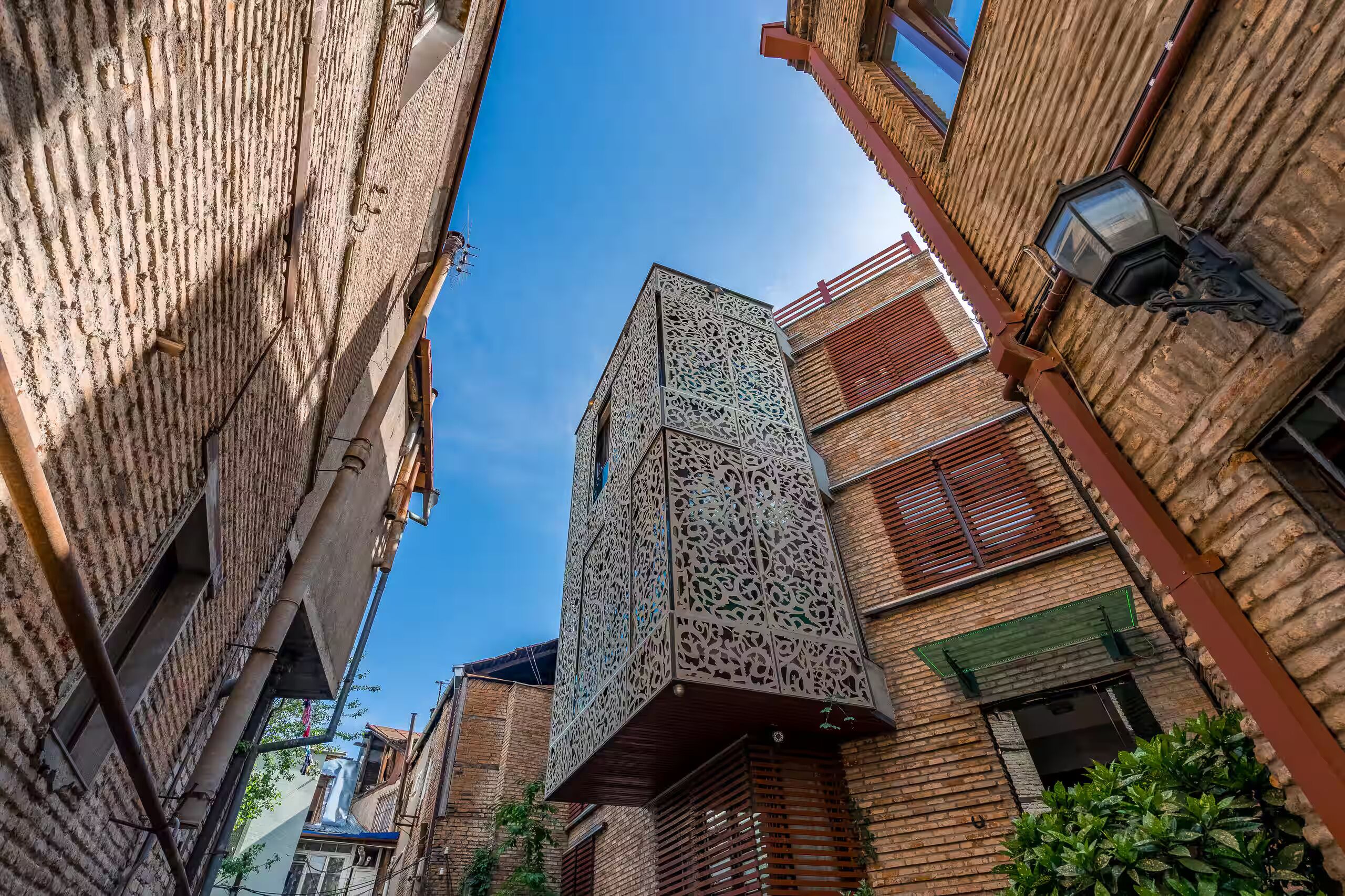 Ein schmaler Gang zwischen traditionellen Backsteingebäuden, eines davon mit einer verzierten Metallfassade.