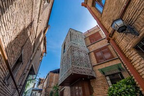 Ein schmaler Gang zwischen traditionellen Backsteingebäuden, eines davon mit einer verzierten Metallfassade.