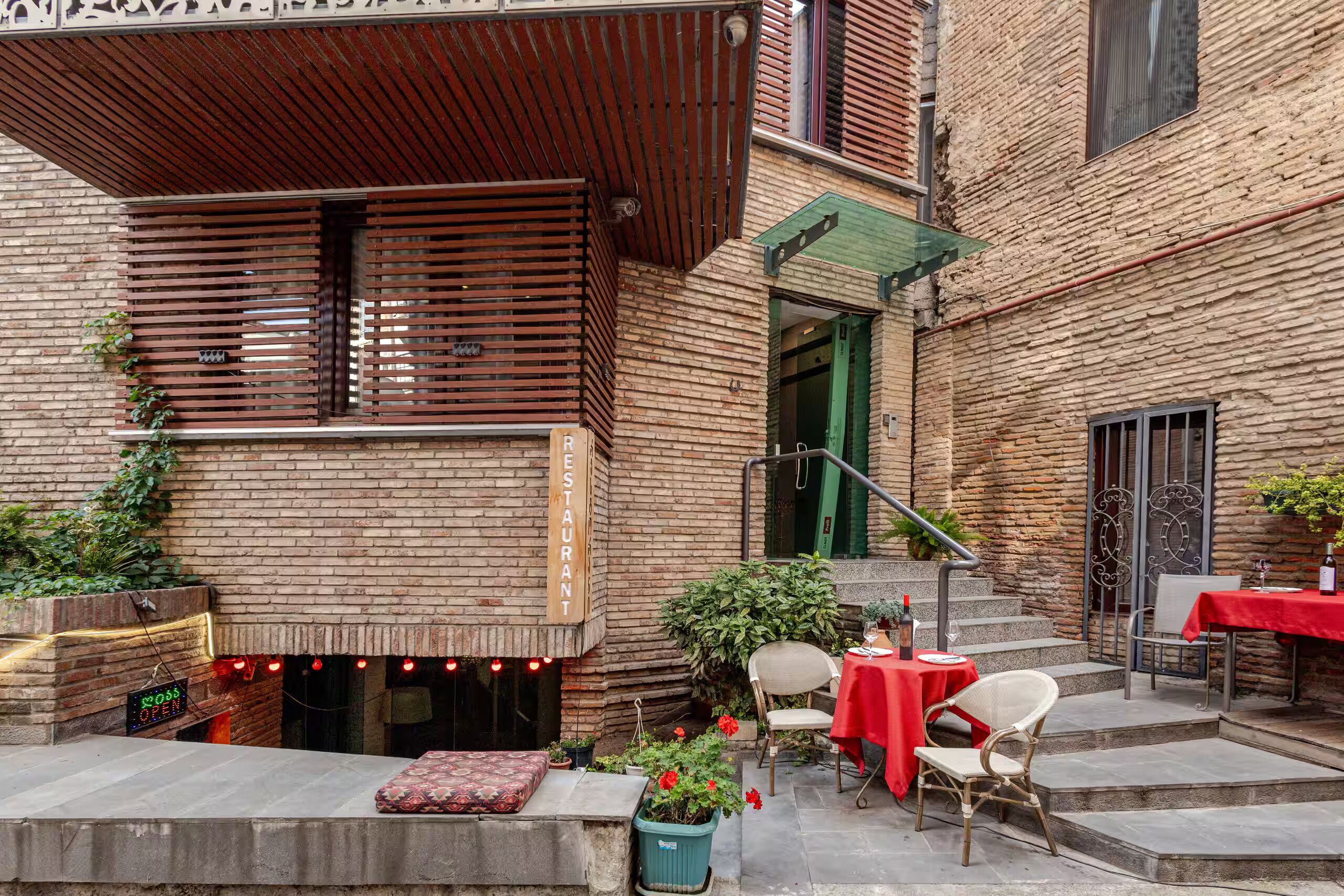Un espace extérieur aménagé avec une table, une nappe rouge, un mur en briques et une pergola en bois.