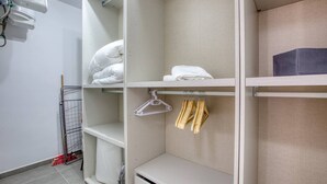 Ein Hotelzimmer mit einem weißen Kleiderschrank, einem Bett mit weißer Bettwäsche und einem kleinen Tisch mit einem schwarzen Gegenstand darauf.