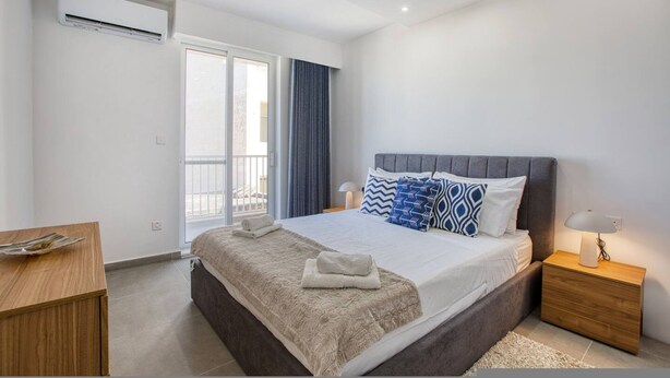 Ein modernes Schlafzimmer mit einem großen Bett, einem Nachttisch, einer Lampe und Blick ins Freie.