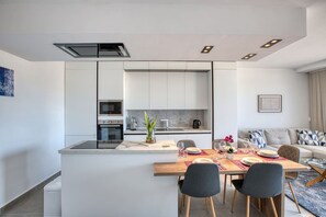 Eine moderne Küche mit eingebauten Geräten, ein Essbereich mit Holztisch und -stühlen sowie ein Wohnbereich mit Sofa und Kissen.