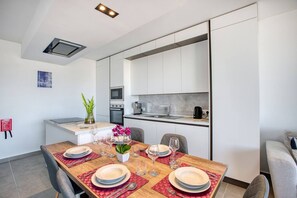 A modern kitchen with a dining area, including a table set for four with plates, glasses, and cutlery. - Xag ra Apartment With Sea Views Balcony Gozo (Xaghra)
