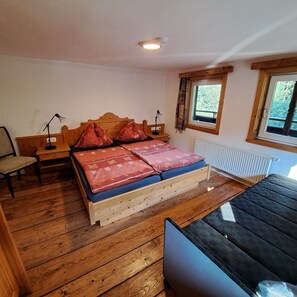 A wooden bed with a headboard, a bedside table with a lamp, a chair, and a window with curtains.