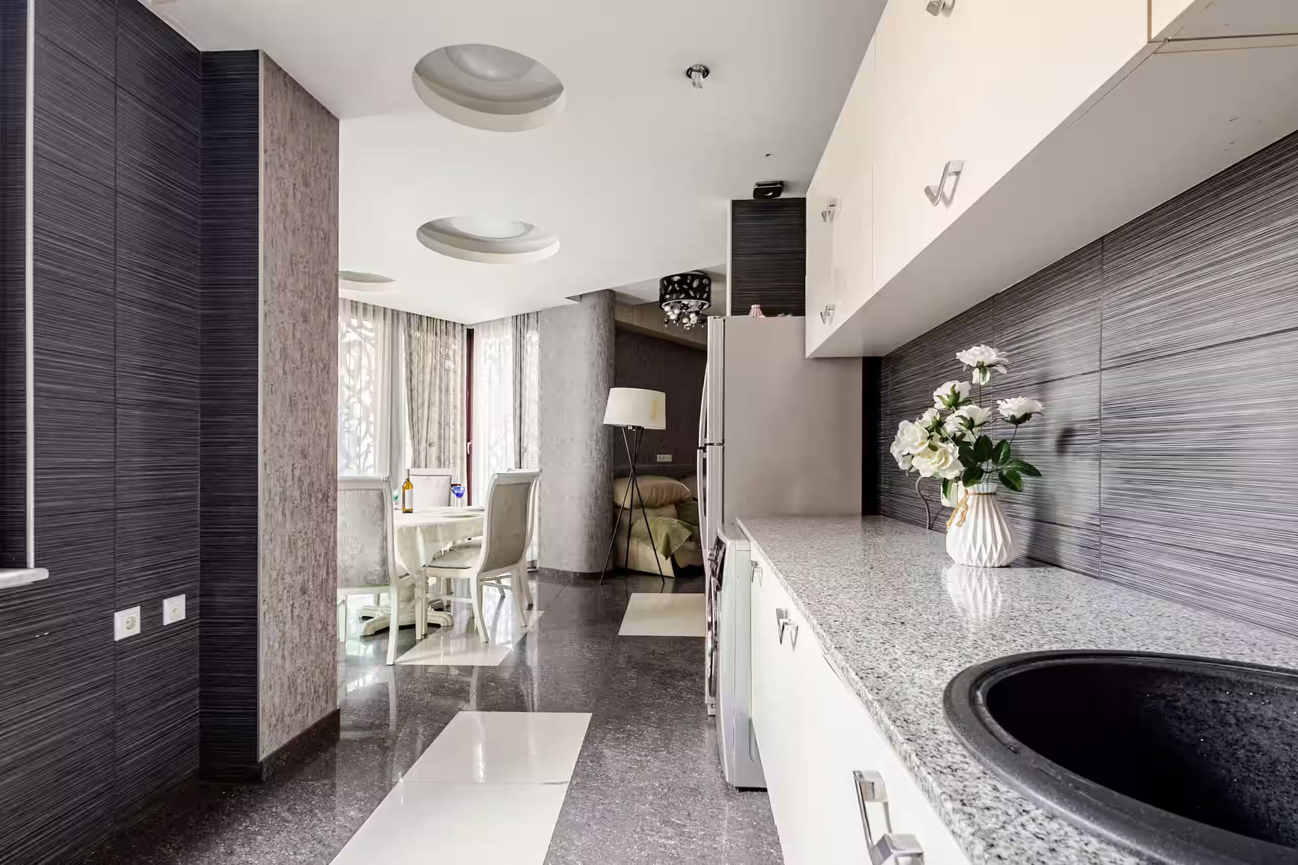 Une cuisine moderne dotée d’un îlot central, un coin repas avec une table et des chaises, et un espace de vie comprenant un canapé et une lampe.