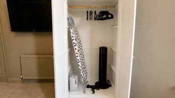 A walk-in closet with a hanging rack, ironing board, and a black cylindrical object.