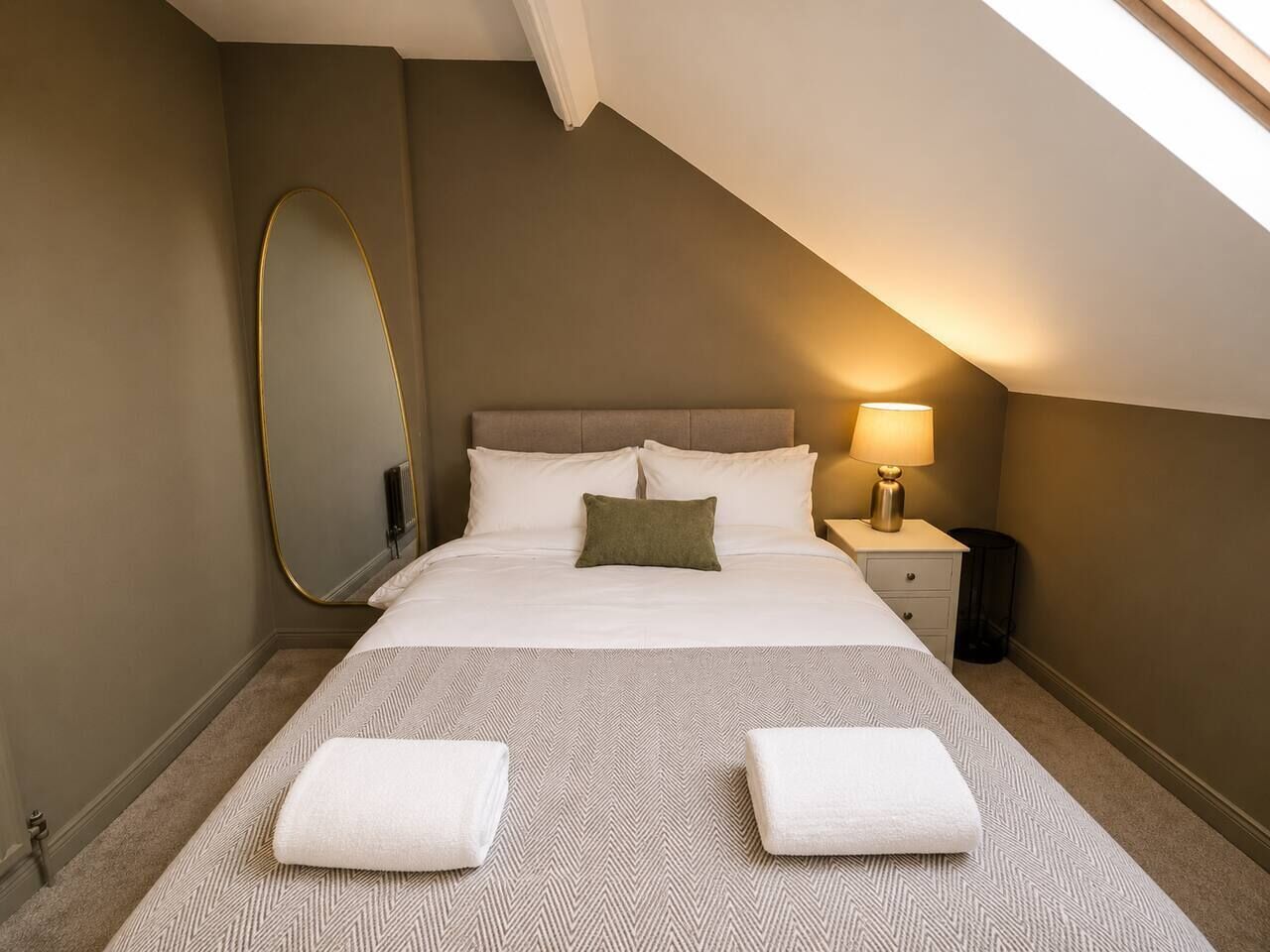 Un dormitorio con cama, mesitas de noche, lámpara, espejo y ventana.