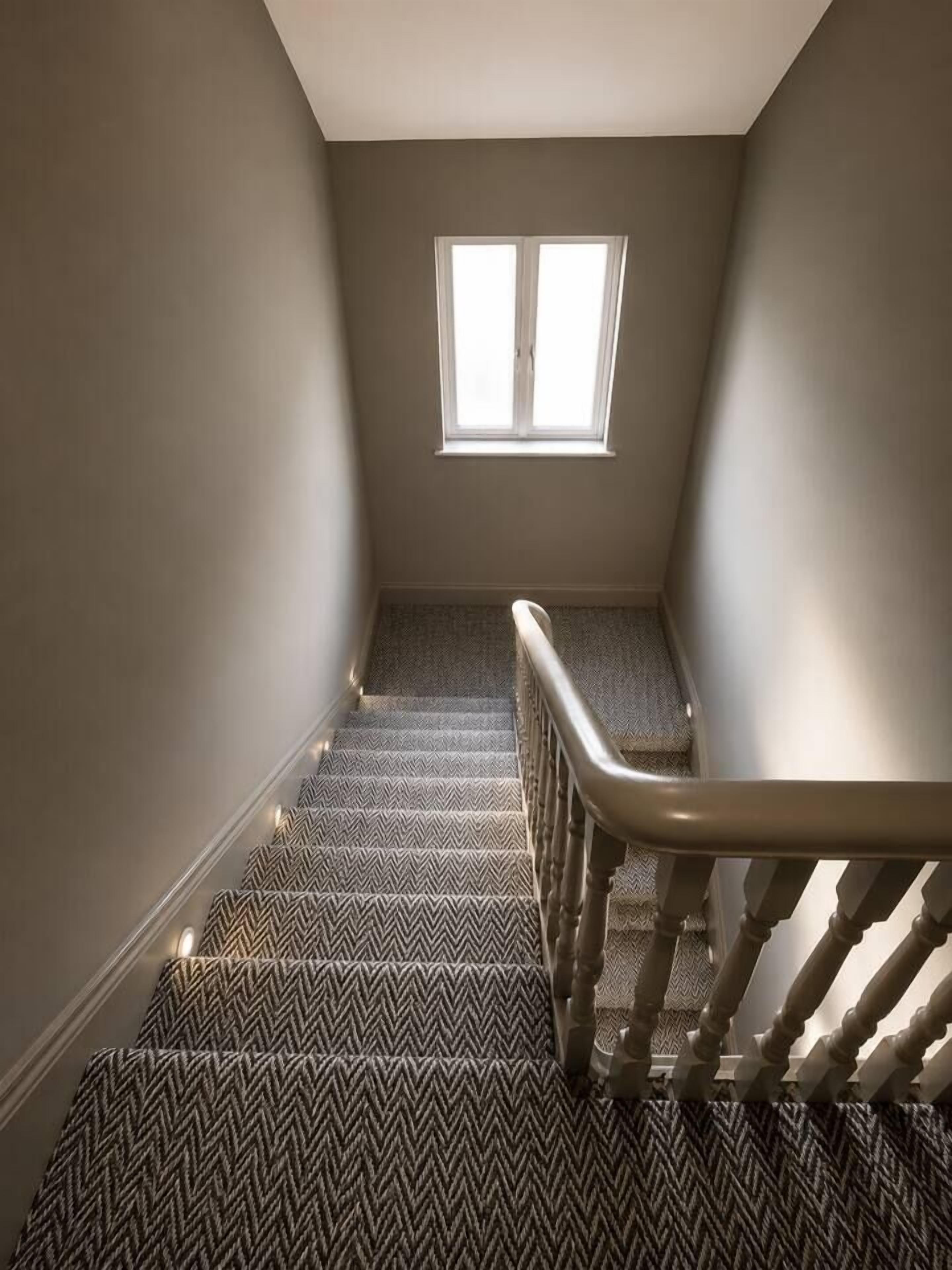 Un escalier recouvert d’une moquette à motifs menant à un palier doté d’une fenêtre.