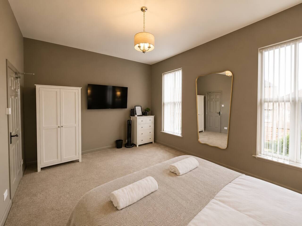 A bedroom with a bed, a wardrobe, a television, a dresser, and a mirror.
