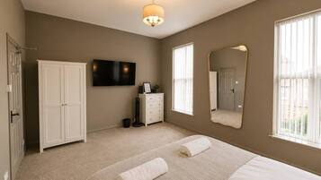 A bedroom with a bed, a wardrobe, a television, a dresser, and a mirror.