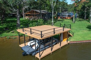 A floating deck with a covered seating area and a small boat docked underneath. - Waterfront 3 bed, 2 bath lake-house on Cedar Creek (Mabank)