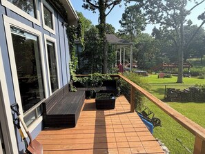 Um deck de madeira com mobiliário de exterior, uma pérgula e vista para um parque.