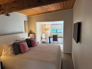 Quarto com uma cama grande, uma escrivaninha e uma TV fixada na parede.