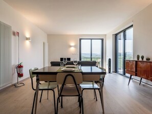 Ein moderner Essbereich mit Tisch für vier Personen, einer Couch, einem Heizkörper, einem Feuerlöscher und Blick ins Freie.