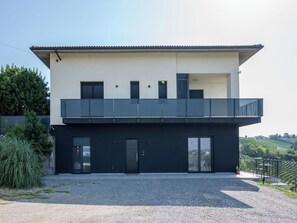 Ein modernes, zweistöckiges Gebäude mit flachem Dach, einem Balkon und einer Schotterauffahrt.