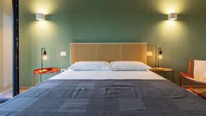 Hotellihuone, jossa on suuri sänky, kaksi yöpöytää, tuoli ja seinään kiinnitetty valaisin.