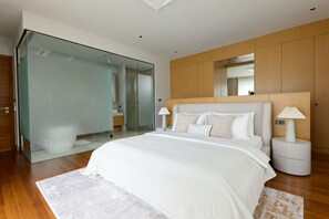 A modern bedroom with a large bed, a glass shower enclosure, and wooden paneling on the walls. - Botanica Pru Jampa New 3BR Pool Villa (ตำบล เทพกระษัตรี)