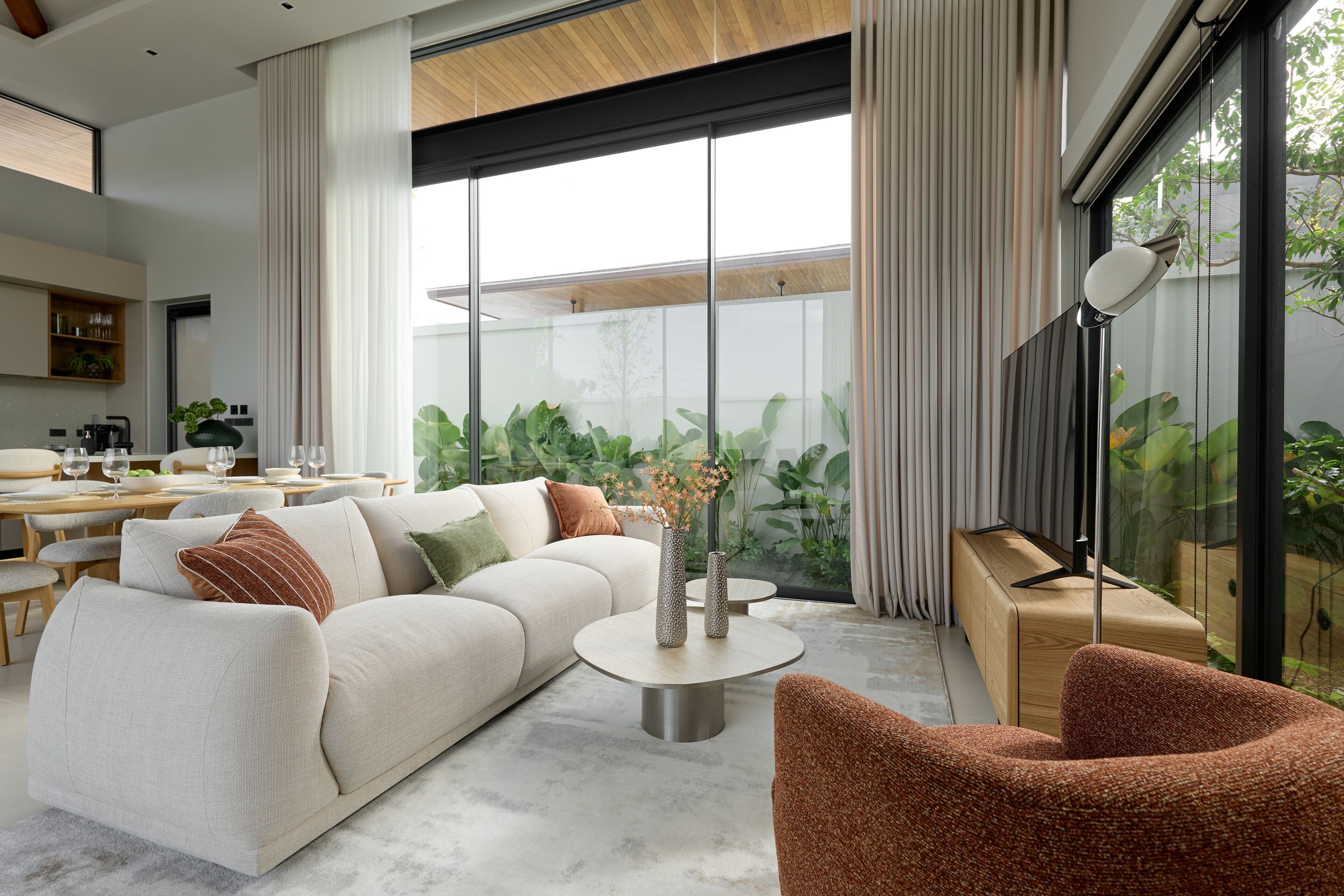 Un salón moderno con sofá, mesa de centro y vistas a la vegetación a través de amplios ventanales.