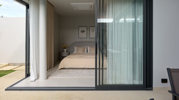 A modern bedroom with a sliding glass door leading to a balcony. - Botanica Pru Jampa New 3BR Pool Villa (ตำบล เทพกระษัตรี)