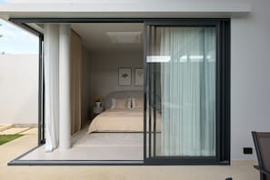A modern bedroom with a sliding glass door leading to a balcony. - Botanica Pru Jampa New 3BR Pool Villa (Thep Krasatti)