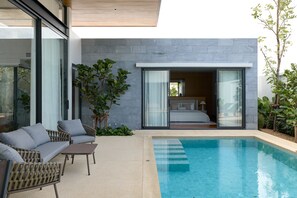 Ein moderner Poolbereich im Freien, durch Glastüren ist ein Schlafzimmer mit Glasfassade sichtbar.