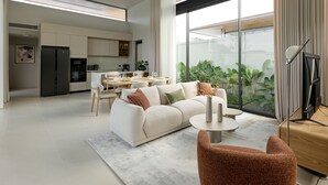 A modern living room with a sofa, coffee table, and chairs, a dining area with a table and chairs, and a kitchen in the background. - Botanica Pru Jampa New 3BR Pool Villa (ตำบล เทพกระษัตรี)