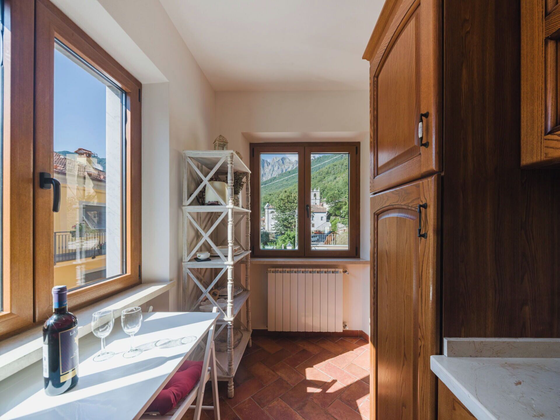 Eine Küche mit Fenster, Holzschränken, einem Heizkörper und einem Tisch mit Flasche und Gläsern.