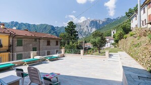 Um terraço com mesas ao ar livre, vista para as montanhas e um edifício com uma torre de sinos.