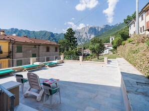 Eine Terrasse mit Sitzgelegenheiten im Freien, Blick auf die Berge und ein Gebäude mit einem Glockenturm.