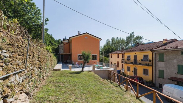 Um bairro residencial com um edifício de dois andares, um muro de pedra e um caminho pavimentado.