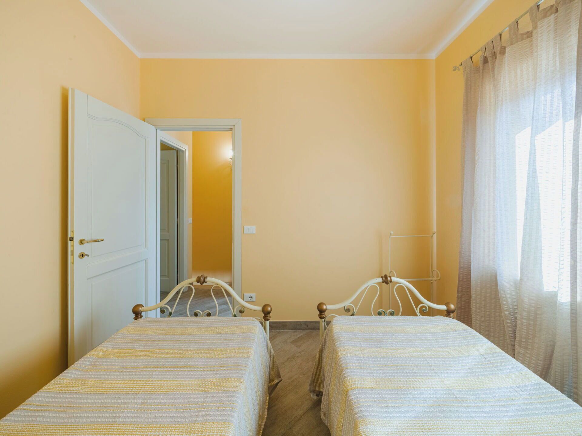 Una stanza con due letti singoli, una porta e una finestra con tende.