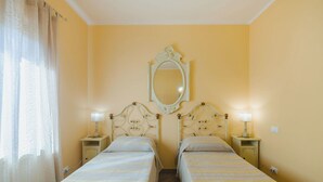 Quarto de hotel com duas camas de solteiro, um espelho grande, abajures e uma janela com cortinas.