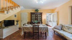 Uma sala de jantar com mesa posta para quatro pessoas, uma televisão num móvel, uma escada e um sofá.