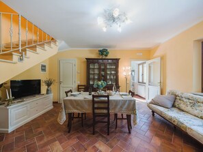 Ein Essbereich mit einem Tisch für vier Personen, einem Fernseher auf einem Schrank, einer Treppe und einem Sofa.