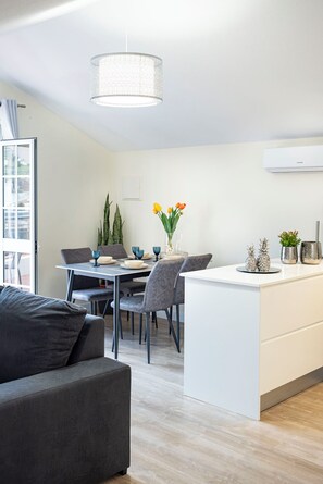 A modern kitchen with a dining area, featuring a central island, grey chairs, and a hanging light fixture. - Cozy Two-Bedroom Attic Retreat: Rooftop, Ocean, and Sunrise Views (Ponta do sol)
