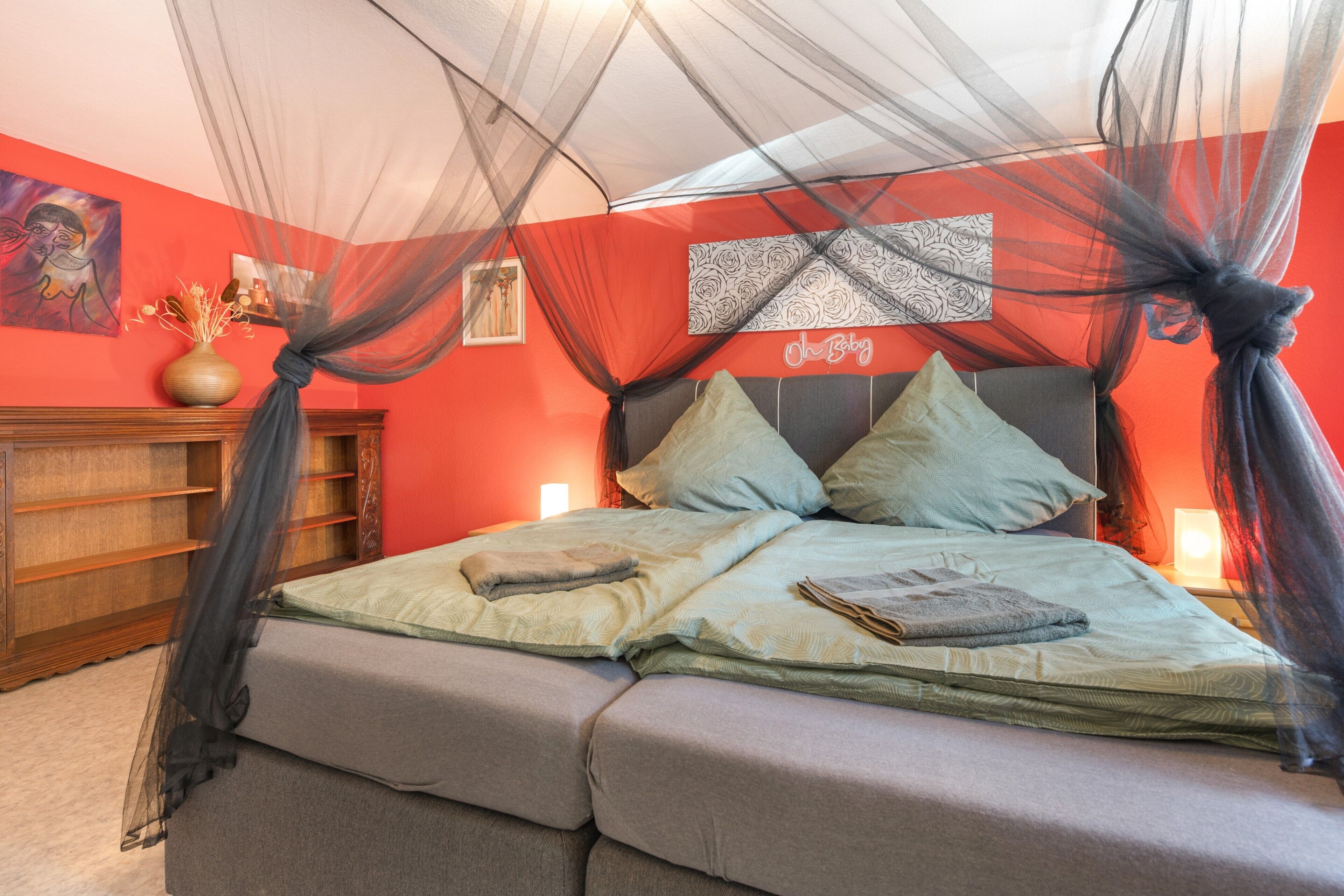 A bed with a canopy, a bedside table, and a wall with a framed picture.