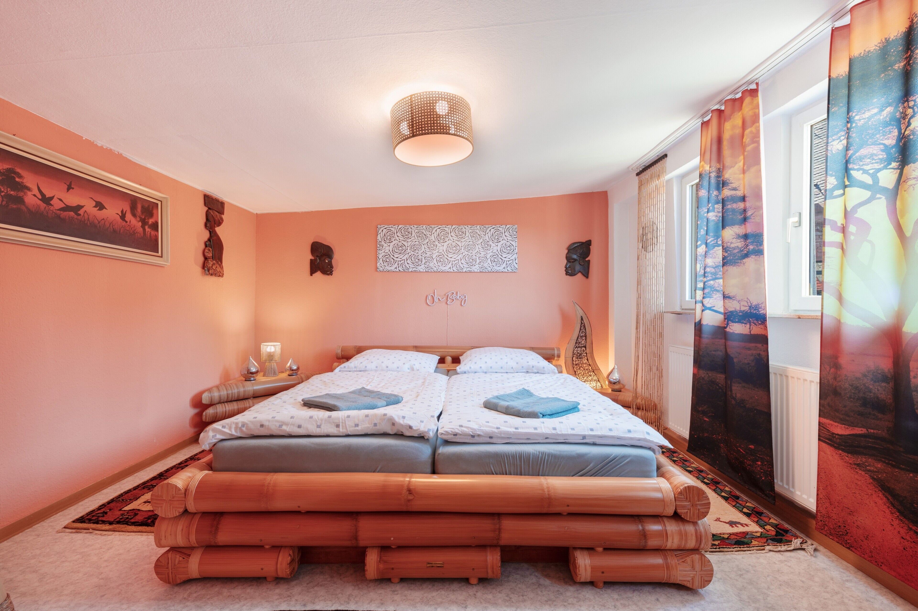 Een slaapkamer met een tweepersoonsbed, een nachtkastje met een lamp, een aan de muur hangend kunstwerk en een raam met gordijnen.