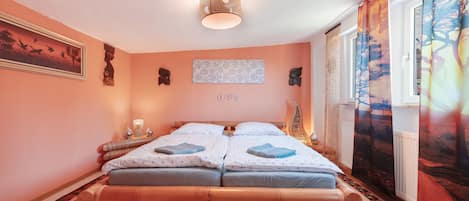 A bedroom with a double bed, a bedside table with a lamp, a wall-mounted artwork, and a window with curtains.