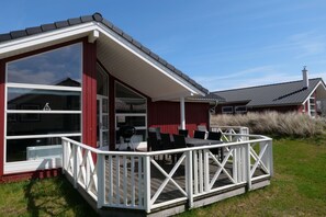 A house with a covered patio, a barbecue grill, and a deck with chairs. - Friedliches Chalet in Grossenbrode (Grossenbrode)