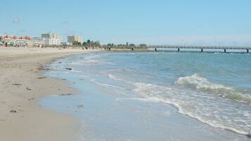 A beach with a pier extending into the water, buildings in the background, and a clear sky.
