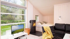 Un interior moderno con un ventanal grande, un sofá negro, una cama y una chimenea.
