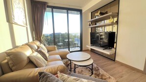 A modern living room with a sofa, a round table, and a TV on a shelf. - 2 Bed Room Rare Unit With Bath Tub Sea View (Pattaya)