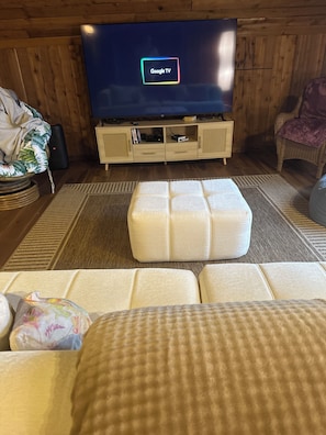 A living room with a television displaying 'Google TV,' a sofa, a patterned rug, and a wicker chair.